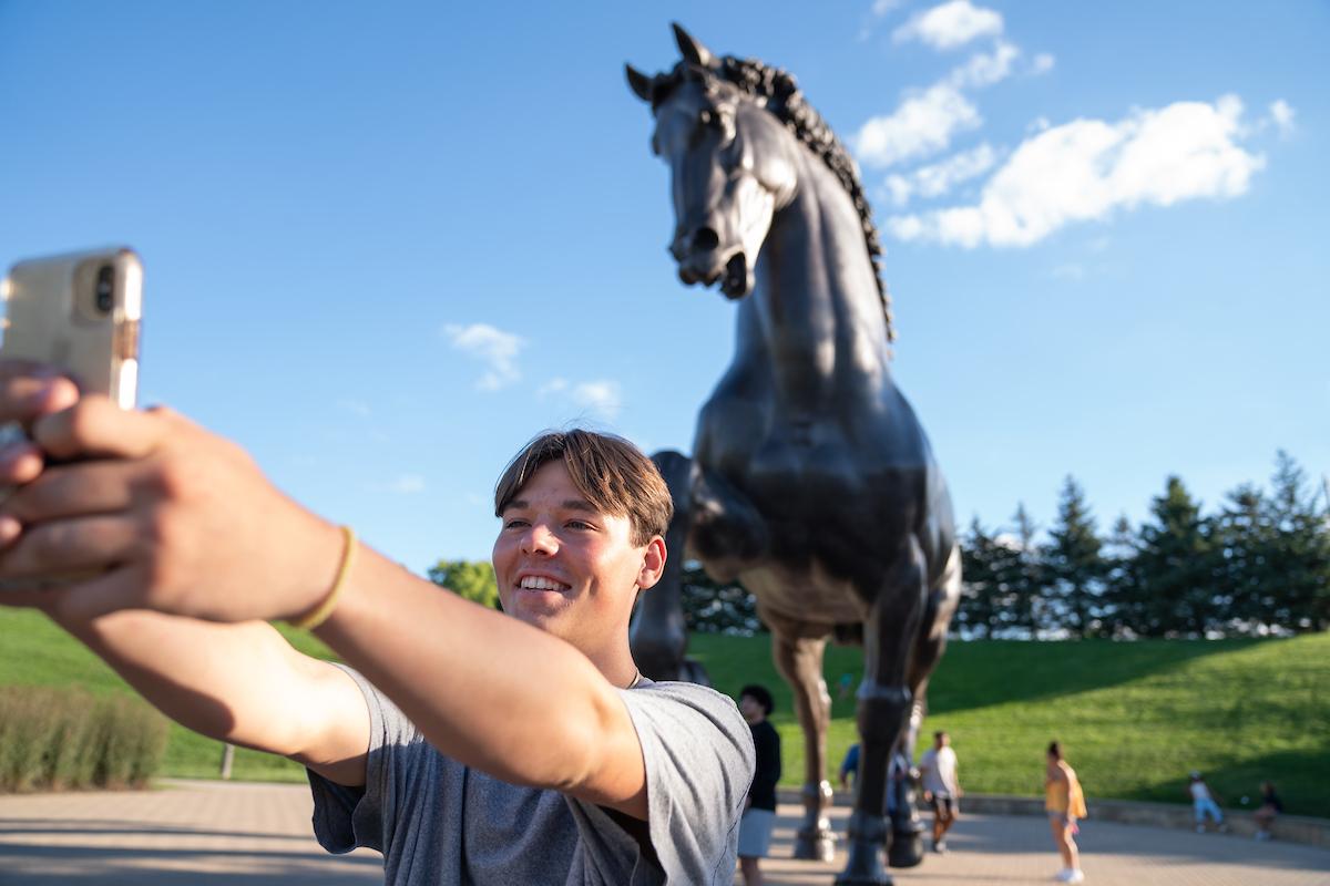 student taking a selfie with 2 story tall horse statue